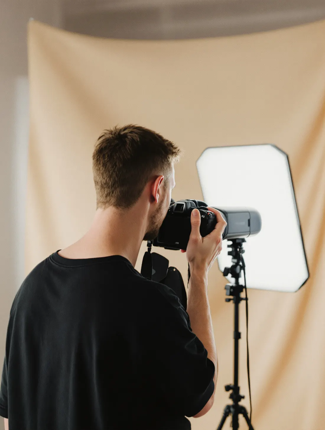 Elliot in his studio, camera raised, beside a speedlight in a large octabox.